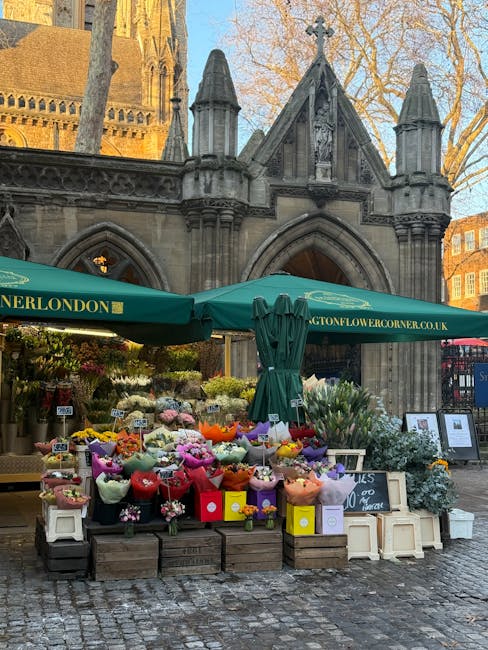 A vibrant flower stall set up outdoors in front of a historic stone building with Gothic architectural features, including pointed arches and decorative spires, under a clear sky with leafless trees i